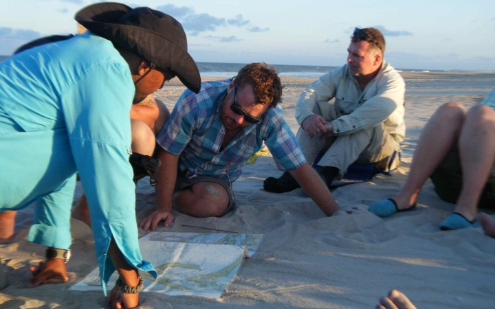 a group of veterans sit on the beach looking at a map